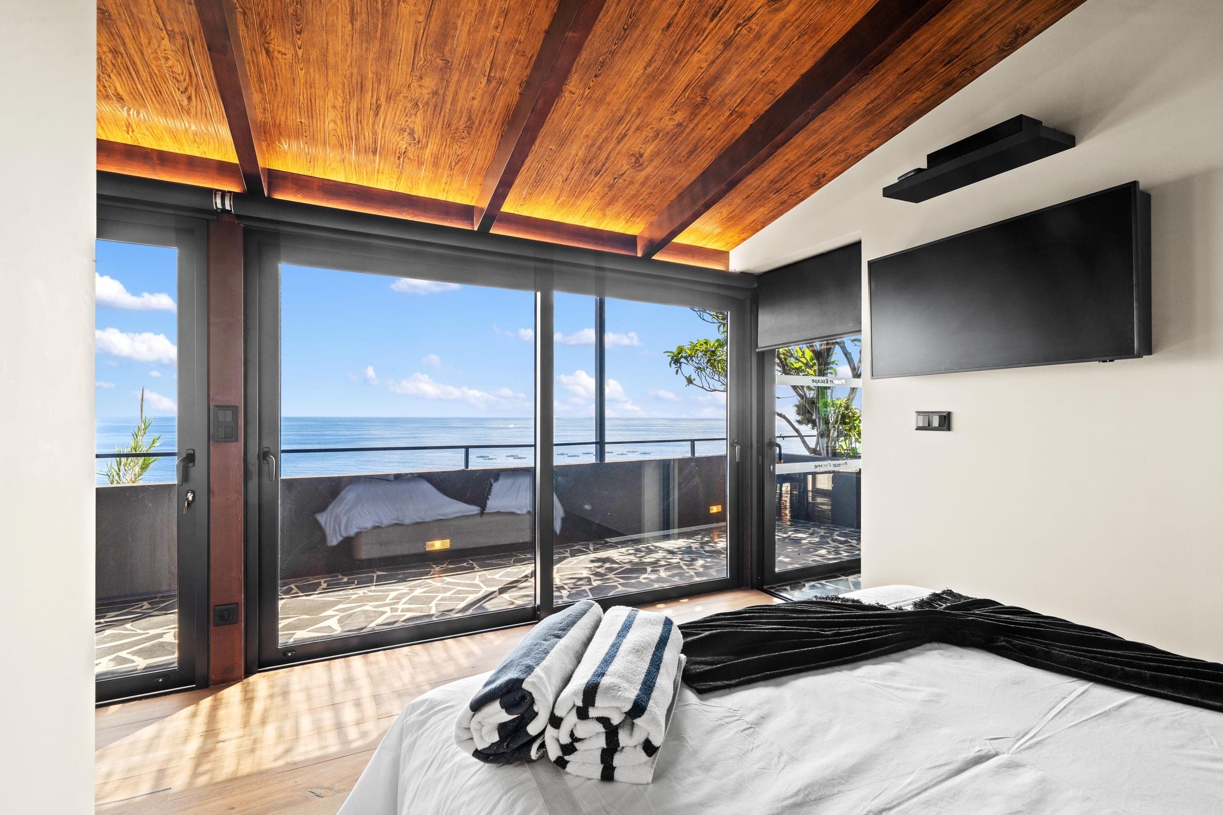 The bedroom's black-framed glass opens straight onto the terrace and sea.