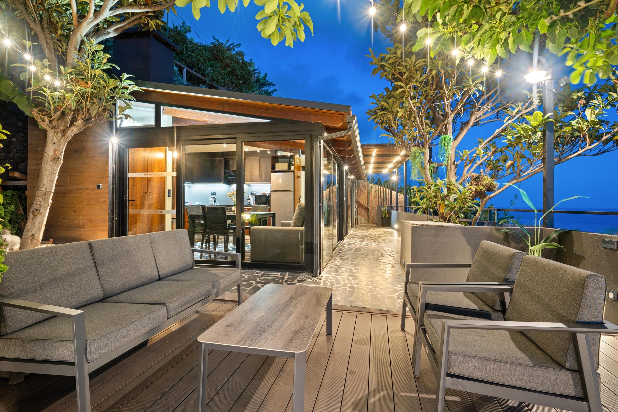 Festoon lights over the terrace at night, the glass doors open onto the kitchen.