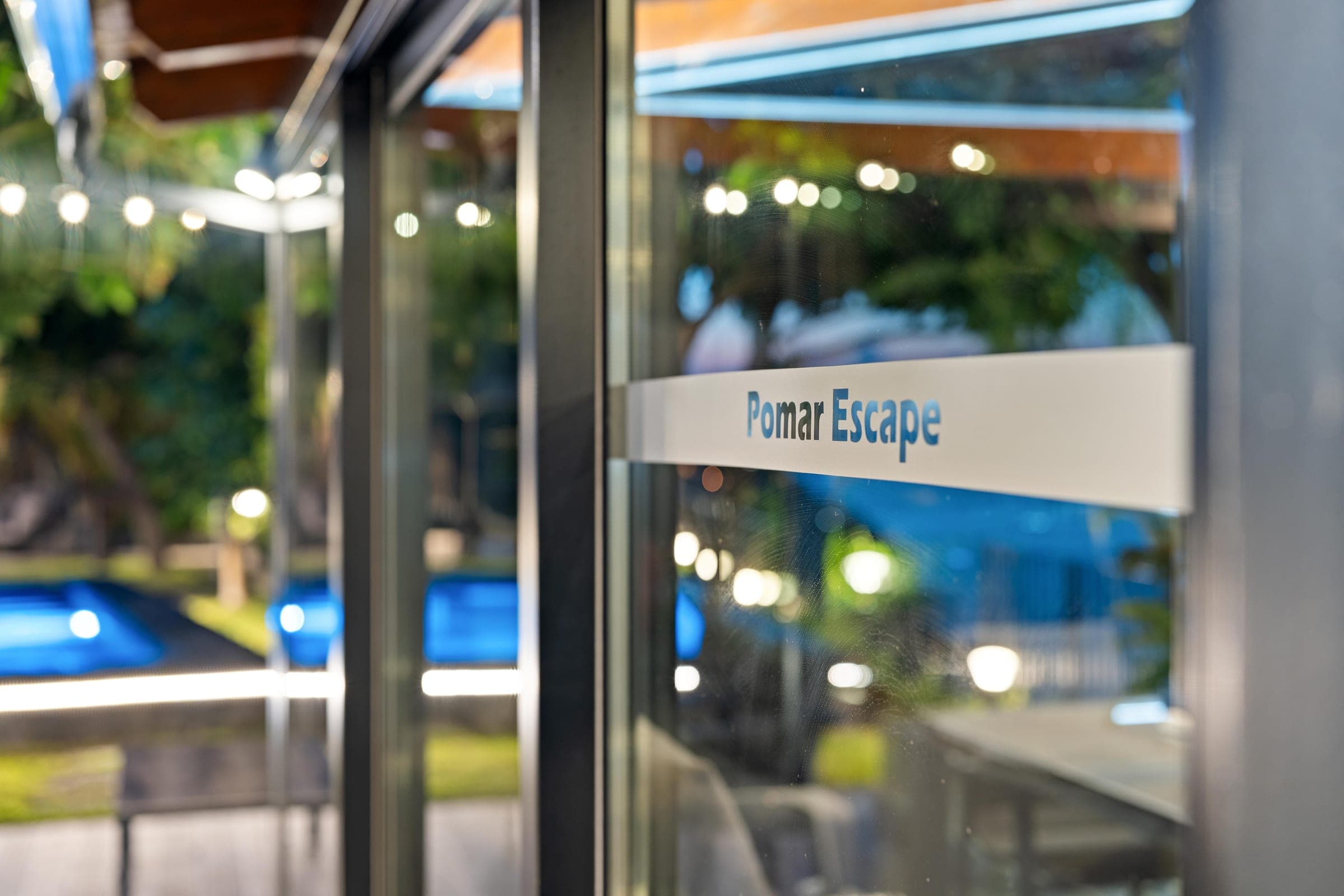 The name Pomar Escape on the glass door, the lit pool reflected behind it.
