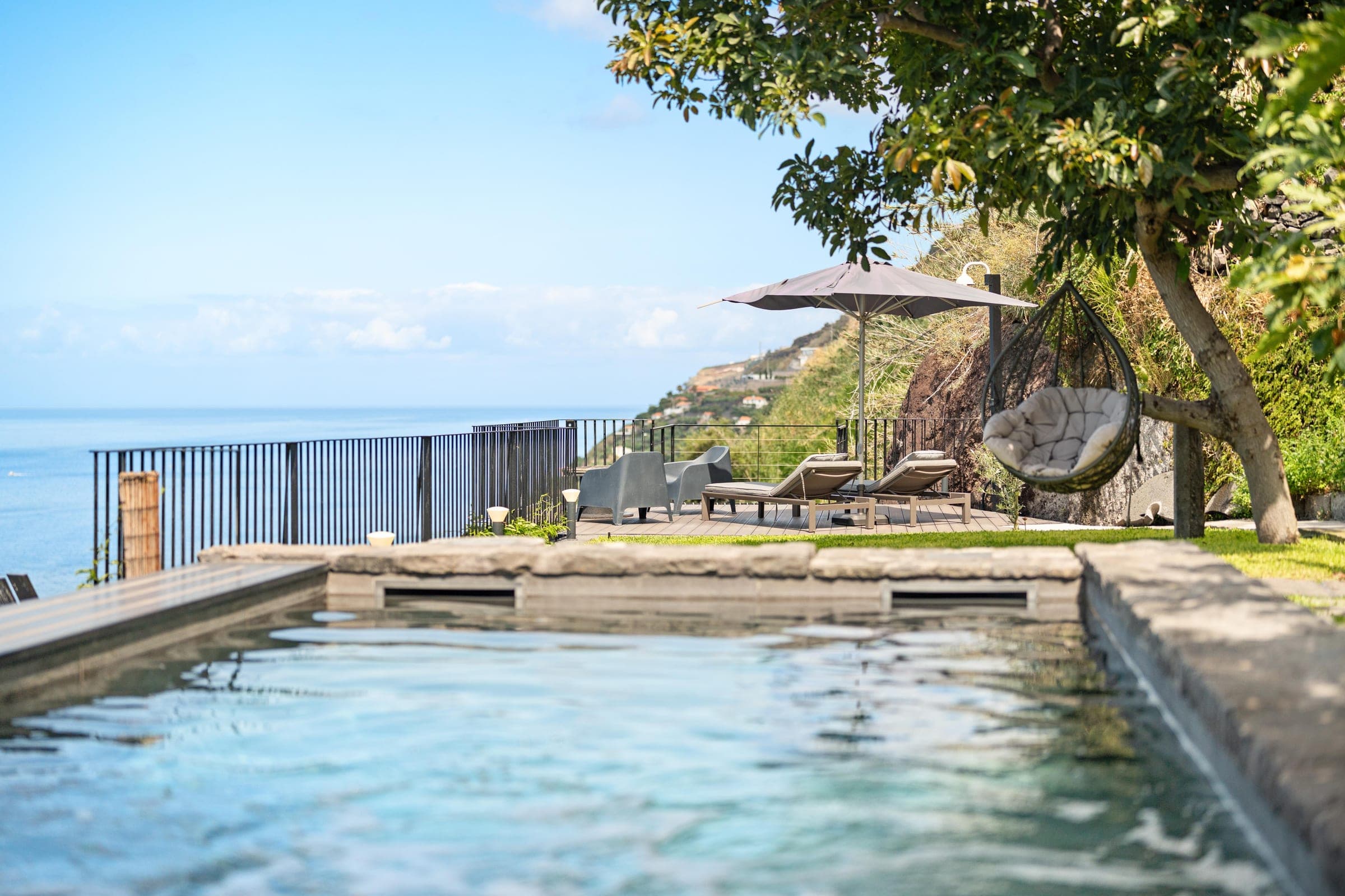 From the water's edge: loungers on the deck and the hanging chair under the tree.