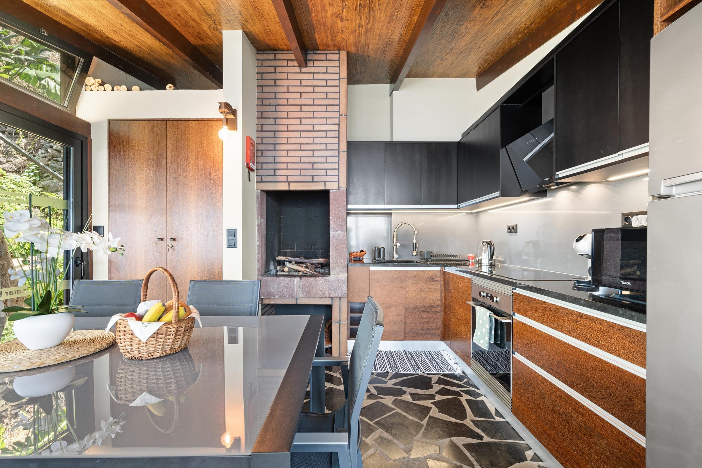 A full kitchen in dark wood and stone, with the old brick fireplace kept in place.
