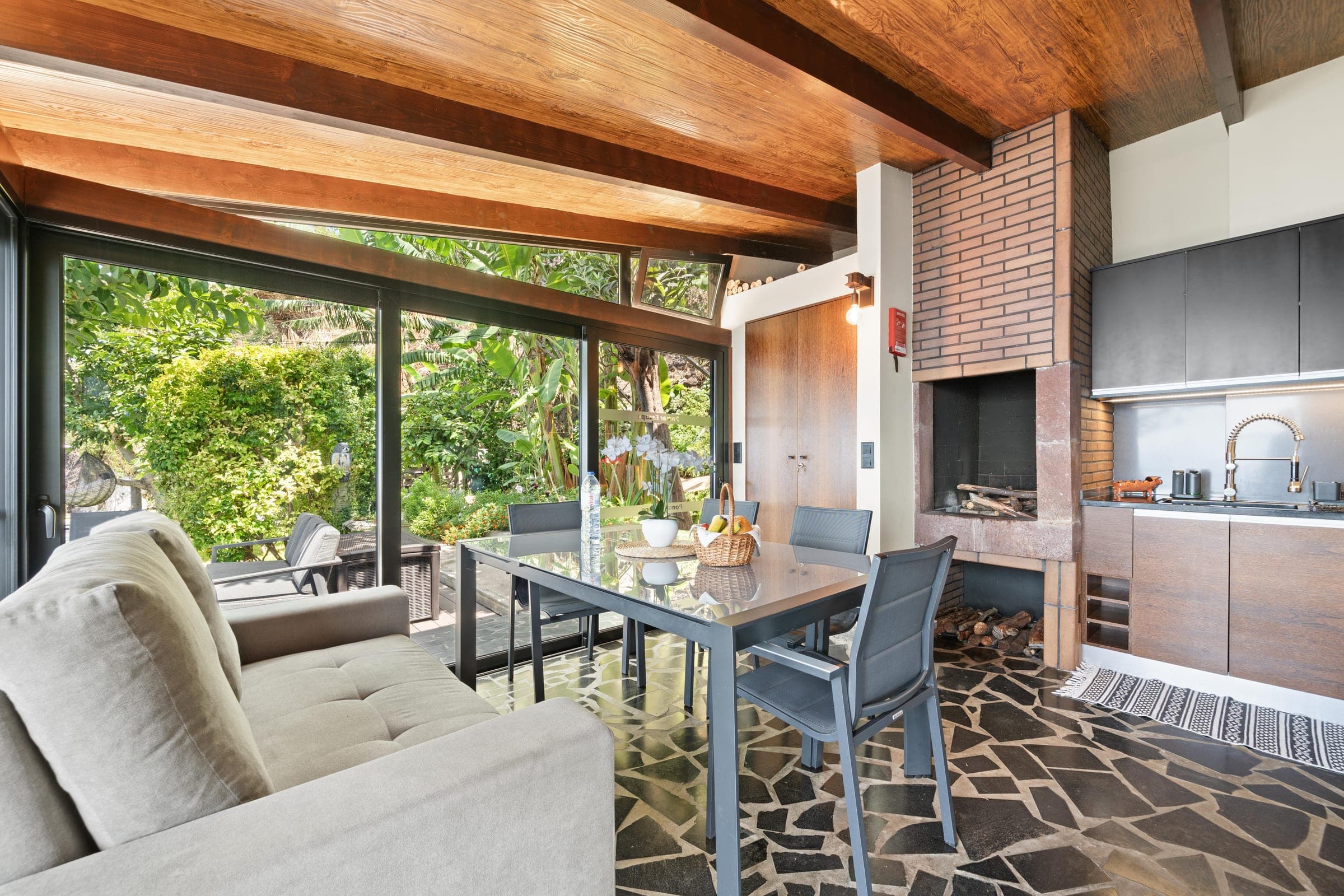 The living room under exposed wood beams: a linen sofa, a brick hearth, and a glass wall onto the garden.