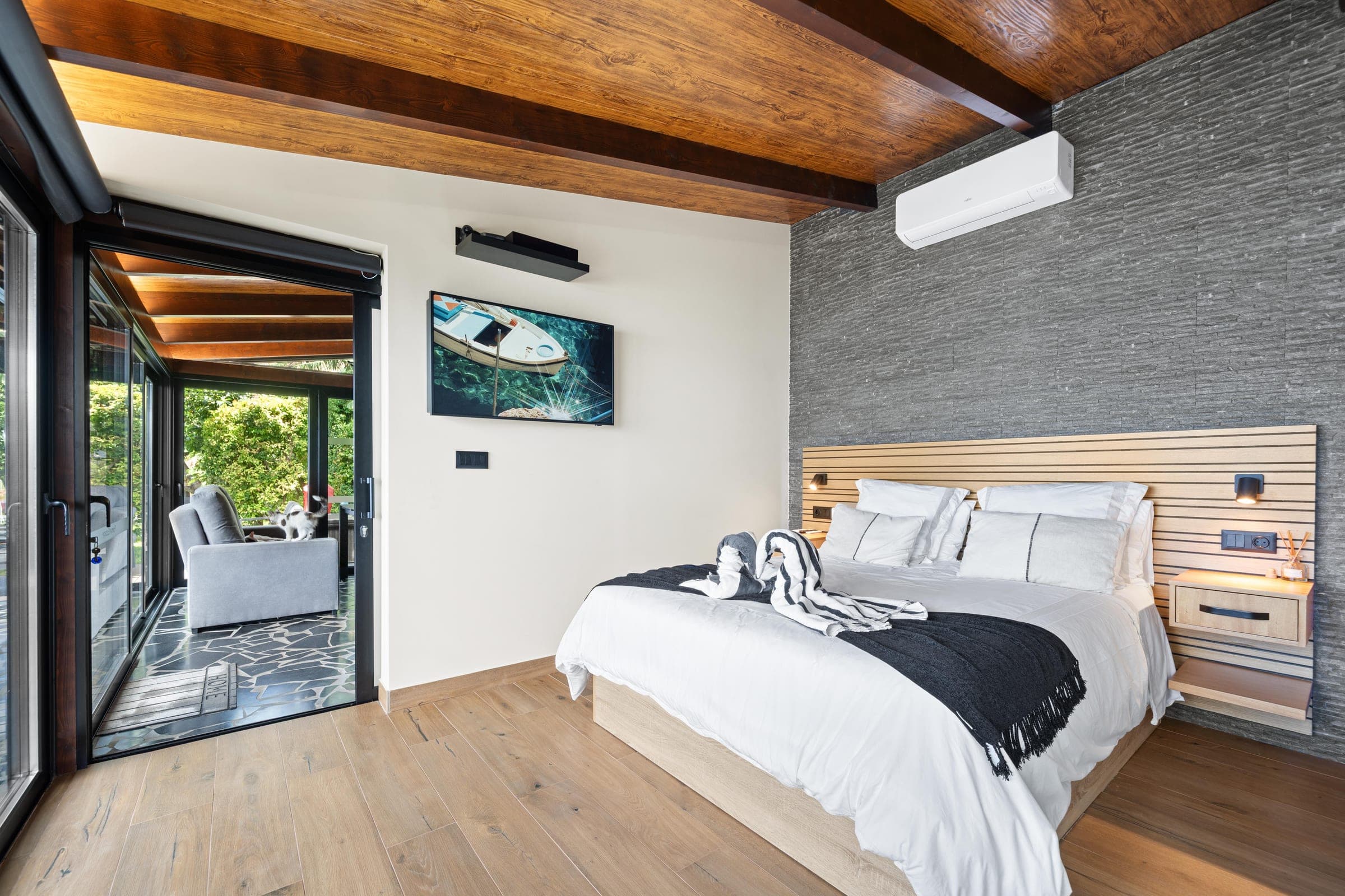 The bedroom door stands open to the glassed lounge among the trees.