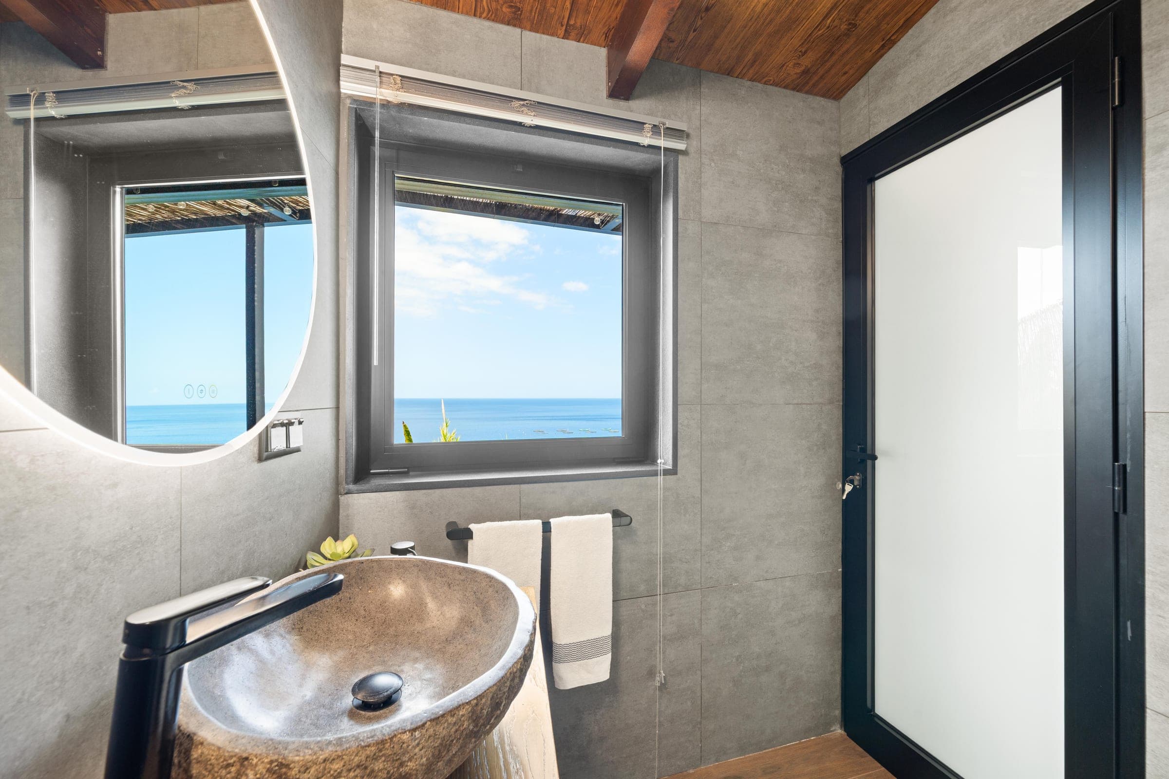 The bathroom, where the round mirror and the window hold the same stretch of ocean.