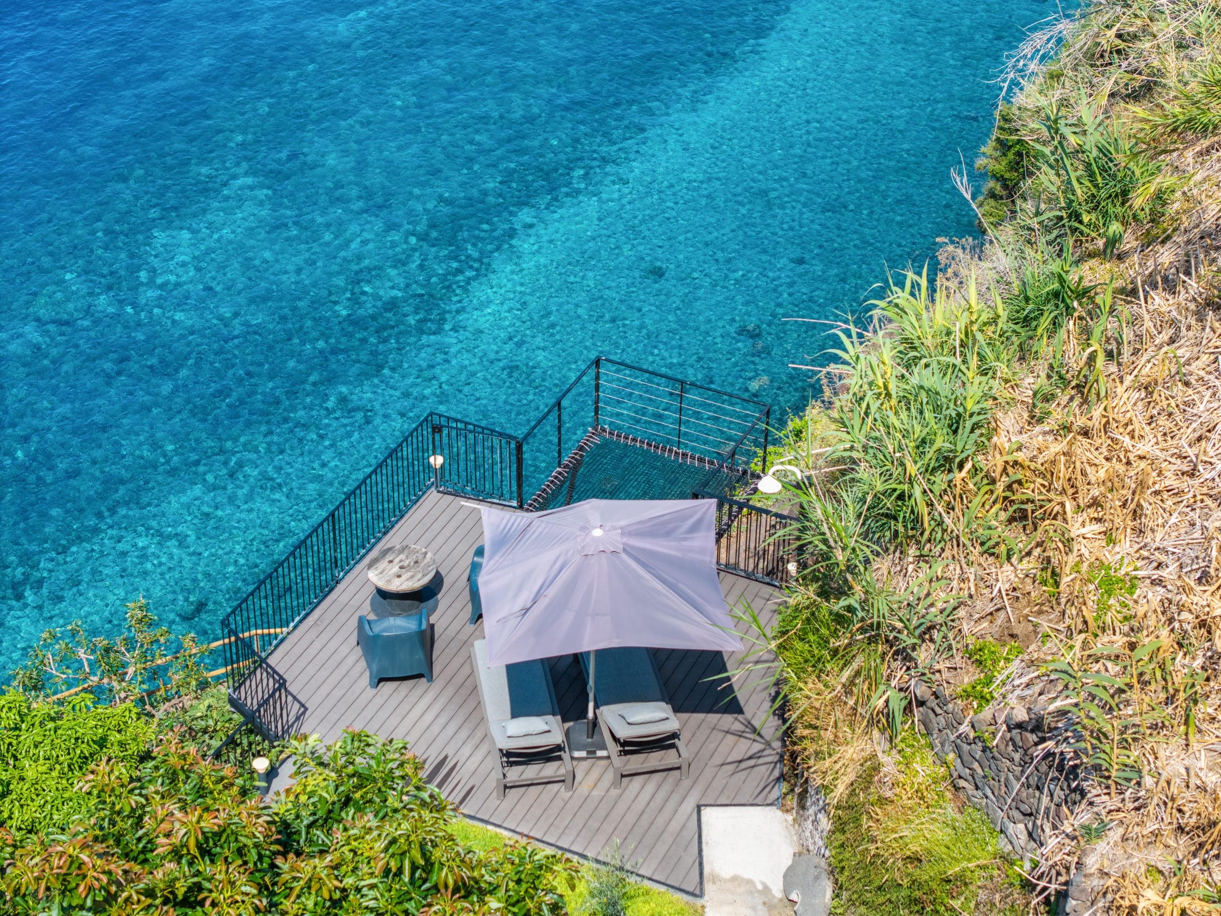 Straight down onto the cliff deck: umbrella, loungers, and clear water far below.