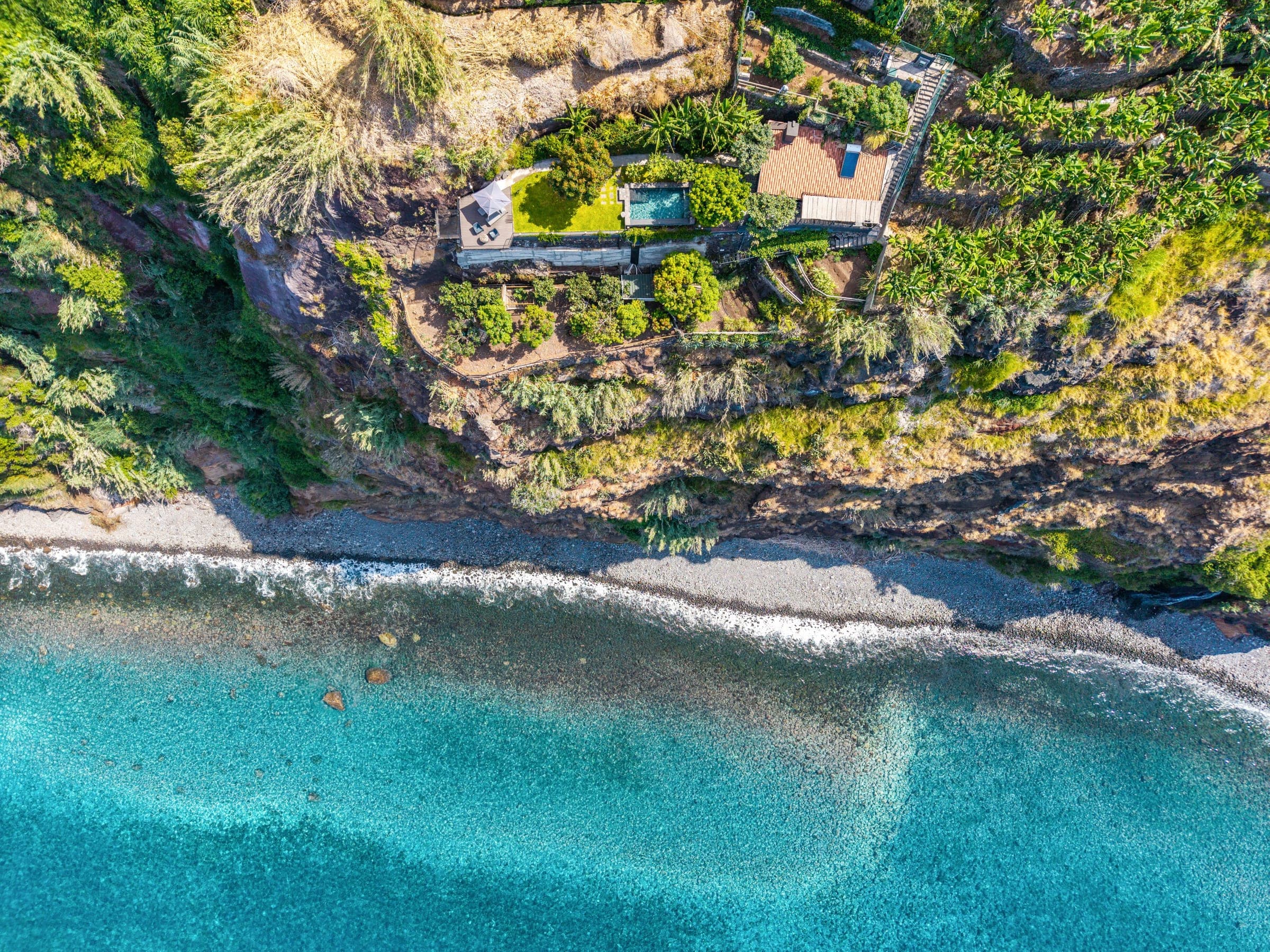 The whole descent from above — house, pool, terraces and the black-pebble shore.